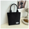 Detalle de bolso tote de pana negra con logotipo sobre escritorio blanco decorado - Negro