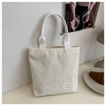 Detalle del bolso tote de pana blanco crema con logo sobre una mesa con estilo - Blanco