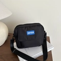Minimalist black canvas crossbody bag featuring a blue rubber logo label on front - Black
