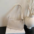 Minimalist beige lychee grain leather underarm bag with silver zipper on a book - White