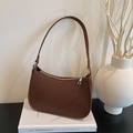 Brown litchi grain leather underarm bag with silver zipper on a white book - Brown