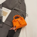 Mini-Umhängetasche in Orange mit silberner Schnalle auf grauem Blazer-Hintergrund - Orange