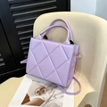 Lavendelfarbene gesteppte quadratische Handtasche mit Schultergurt auf dem Stuhl - Lila