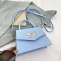 Light blue crossbody bag with silver bow accent and matching top handle on denim - Blue