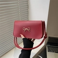Red leather handbag with a gold bow buckle shown in a lifestyle office setting - Red