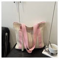 Detail of hand-woven straw tote bag with pink canvas handles and tassel charm on wood table - Pink