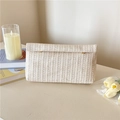 Schicke beige gewebte Umschlag-Clutch auf einem Schreibtisch mit eleganten Tulpen - Beige