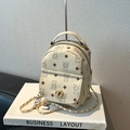 Mini cream backpack with brown bear pattern and gold chain strap on display - White