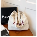 Detail of off-white canvas tote bag with brown Beach lettering and drawstring closure - White