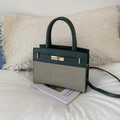 Detail van donkergroene leren en beige canvas handtas met goudkleurig slot op boek - Groen