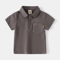 Dettaglio polo grigio scuro da bambino con bottoni in legno e etichetta sulla tasca - 90cm / caffè