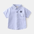 Dettaglio camicia celeste da bambino con taschino e ricamo lettera B sulla parte frontale - Celeste / 90cm