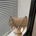 Bolso baguette beige elegante con cadena plateada y colgante de lazo frente a una ventana - Caqui