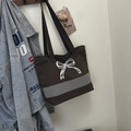 Detail of a dark brown canvas tote bag featuring white bow embroidery and black straps - Brown