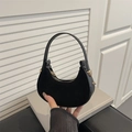 Minimalist black faux suede hobo bag with leather trim and gold hardware held by a person - Black