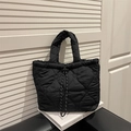 Bolso tote acolchado negro con bordado de corazones y cierre de cordón sobre un libro - Negro