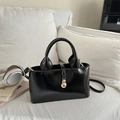 Chic black patent leather tote bag with gold charm on a white minimalist sofa - Black