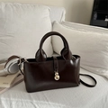 Dark brown high-shine tote bag with gold charm and detachable strap on a white sofa - Dark Brown