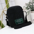 Minimalist black corduroy crossbody bag with green label and wide fabric shoulder strap - Black
