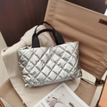 Close-up of a silver quilted tote bag with metallic finish resting on an outdoor chair - Silver
