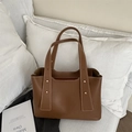 Bolso tote de cuero marrón con remaches dorados y pespuntes en un ambiente de estilo de vida - Marrón
