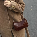Detail of a glossy brown hobo bag with silver chain strap shown in a stylish winter street setting - Coffee