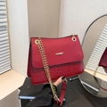 Red shoulder bag with crocodile embossing and golden chain strap in a fashion mirror view - Red