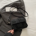 Classic black woven leather crossbody bag with adjustable strap on a gray blazer - Black