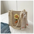 Dettaglio di una borsa tote in paglia intrecciata con ciondolo floreale e foulard decorativo - Bianco
