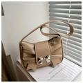 Detailed shot of khaki pleated underarm bag with silver bow buckle on white books - Khaki