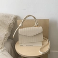 Detail of cream woven crossbody bag with texture and golden hardware on a wooden table - White