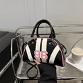 Bolso bowling de rayas negras con número 96 y borde rosa en un estante de metal - Negro