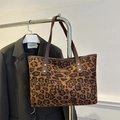 Leopard print tote bag with brown leather handles and gold brand plaque on a dark coat - Brown