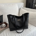 Minimalistische schwarze Shopper-Tasche mit goldenem Schleifen-Detail in Wohnzimmer-Szene - Einheitsgröße / Schwarz