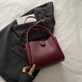 Chic burgundy bucket bag with round handles and adjustable shoulder strap on a suit blazer - Red