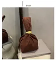 Detail der braunen Wildleder-Beuteltasche mit goldenem Metallgriff auf grauen Büchern - Braun