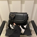 Classic black leather saddle crossbody bag with wide strap and gold hardware on chair - Black