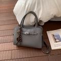 Détail du sac cabas gris en cuir grainé avec fermoir argenté sur sol en bois - Gris Avec Pendentif Bretzel Boulier