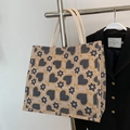 Beige tote bag with grey hearts and yellow floral patterns on a woven linen surface - Large / Black