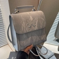 Gray textured leather backpack with silver butterfly clasp shown in a lifestyle setting - Silver