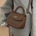 Brown matte PU leather saddle bag with gold lettering and top handle on grey coat - Brown