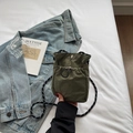 Detalle del mini bolso bandolera de nailon verde militar con cordón y correa tejida en cama blanca - Verde