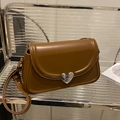 Brown leather saddle bag with silver heart buckle and adjustable strap in lifestyle setting - Brown