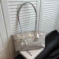 Silver snakeskin shoulder bag with pearl bow pendant on white books background - Silver With Heart Pearl Bow Charm
