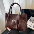 Dunkelbraune geflochtene Lederhandtasche mit Zierschnalle und rundem Griff in Home-Office-Umgebung - Braun