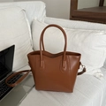 Brown faux leather bucket bag with top handles and fashion logo on white sofa - Tan