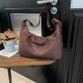 Brown matte suede crescent tote bag with adjustable strap hanging on a wooden door - Brown