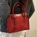 Rote Damenhandtasche mit Materialmix und gelbem Logo an einer Frau in grauem Pullover - Rot