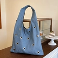 Dunkelblaue Denim-Tragetasche mit silbernen Metallösen auf einem hölzernen Cafétisch - Blau