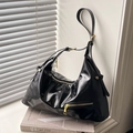 Glossy black underarm bag with gold hardware and adjustable strap on an elegant window sill - Black